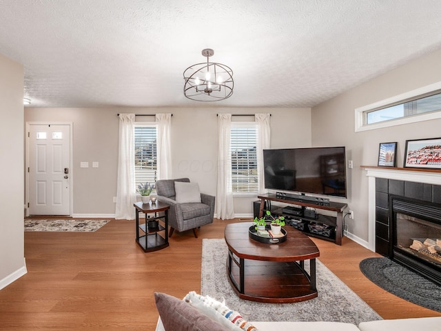 living area featuring a tiled fireplace, baseboards, light wood finished floors, and a textured ceiling