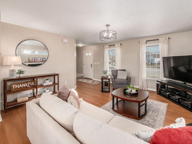 living room featuring wood finished floors, baseboards, a chandelier, and a textured ceiling