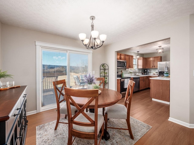 dining area featuring a chandelier, baseboards, a textured ceiling, and wood finished floors