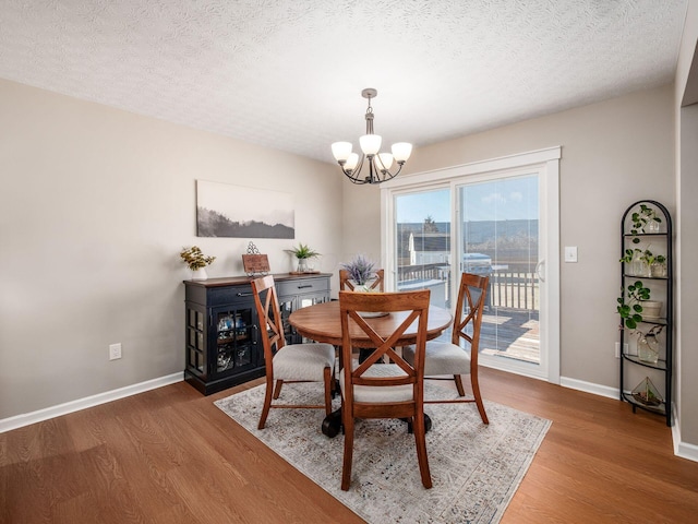 dining room with a chandelier, a textured ceiling, baseboards, and wood finished floors