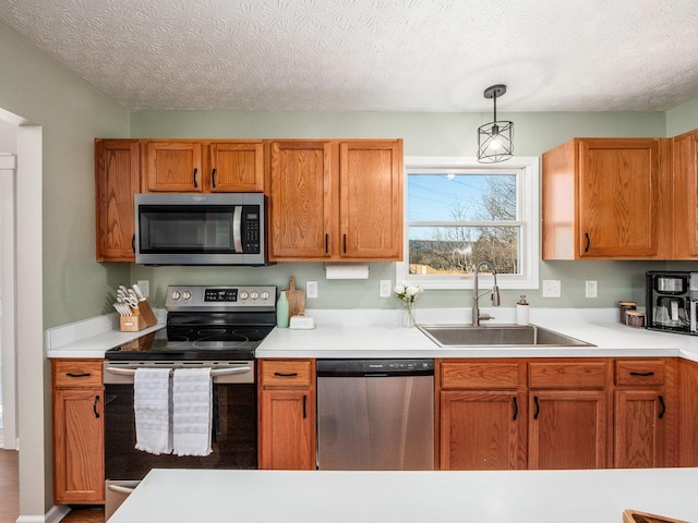 kitchen with decorative light fixtures, light countertops, appliances with stainless steel finishes, a textured ceiling, and a sink