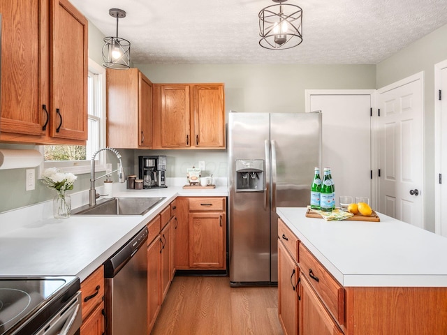 kitchen with light wood finished floors, light countertops, appliances with stainless steel finishes, a textured ceiling, and a sink