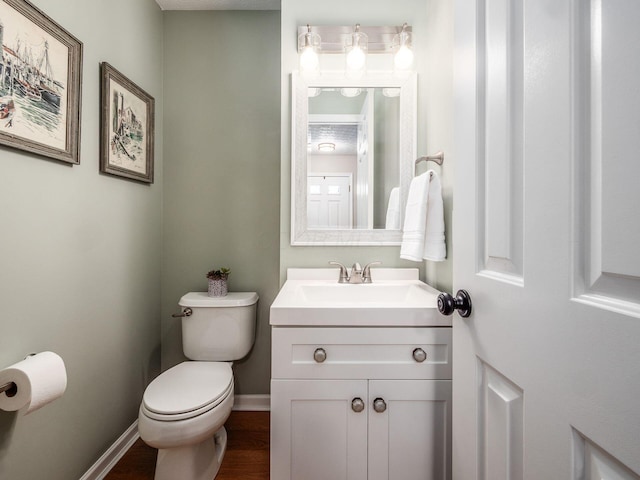 half bathroom with toilet, vanity, baseboards, and wood finished floors