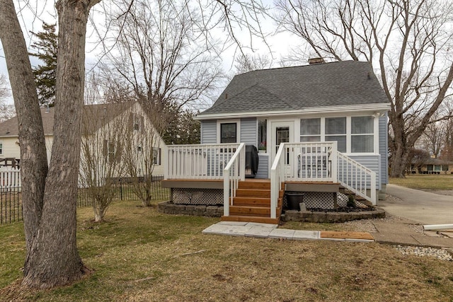 view of front of house with a chimney, roof with shingles, fence, a deck, and a front yard