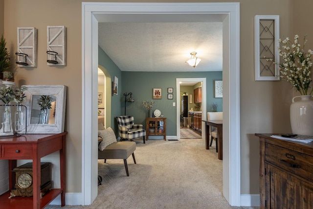 sitting room featuring arched walkways, carpet flooring, a textured ceiling, and baseboards