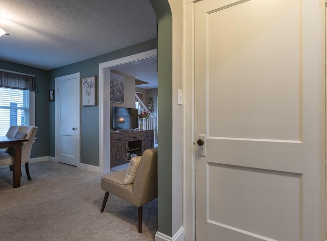 interior space featuring a textured ceiling, carpet, arched walkways, and baseboards