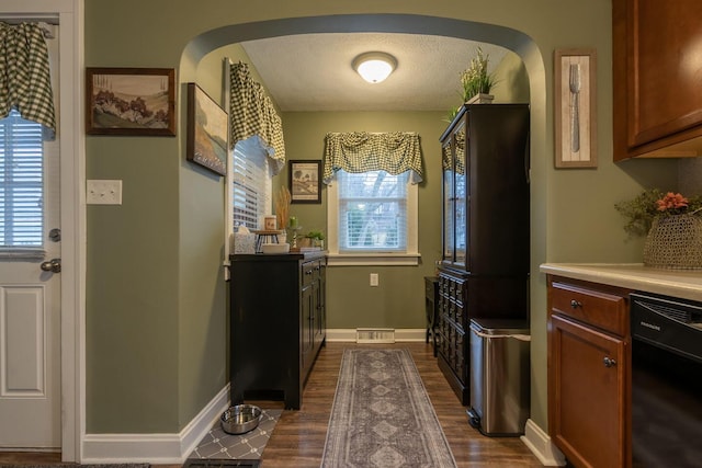 kitchen with arched walkways, a textured ceiling, dark wood-style flooring, baseboards, and black dishwasher