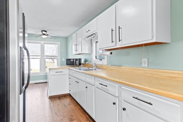 kitchen with stainless steel appliances, wood finished floors, a sink, white cabinets, and light countertops