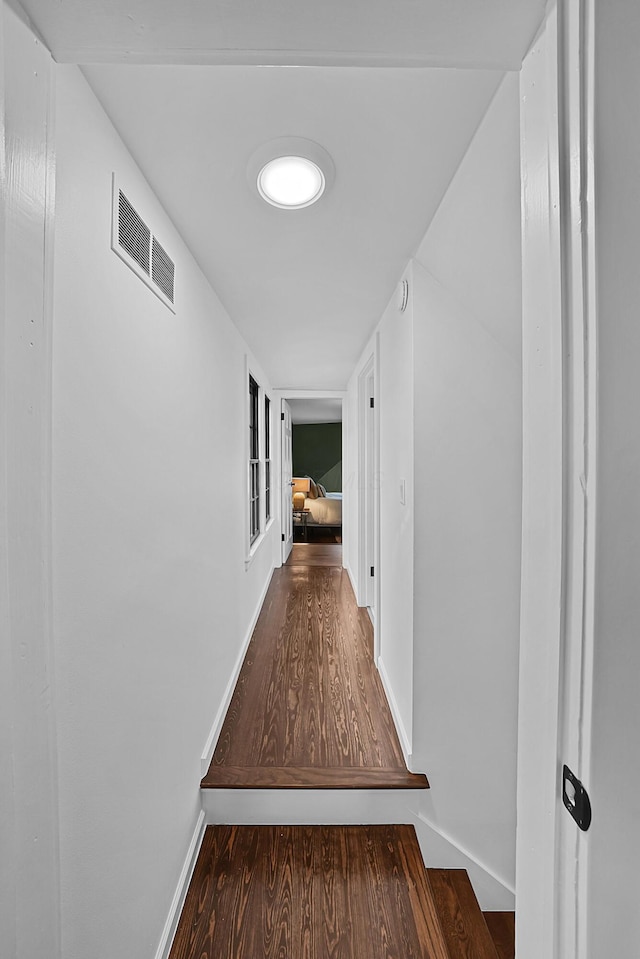 hallway with wood finished floors, visible vents, and baseboards