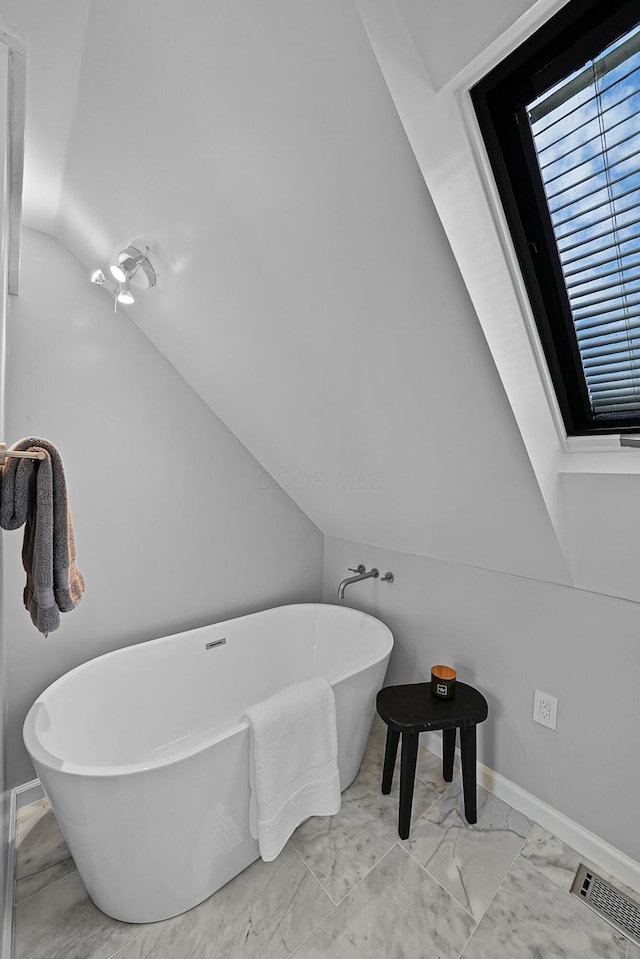 bathroom with marble finish floor, lofted ceiling, visible vents, a freestanding bath, and baseboards