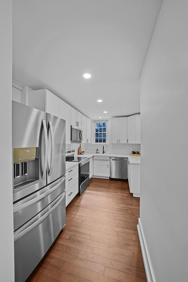 kitchen featuring dark wood finished floors, appliances with stainless steel finishes, backsplash, white cabinetry, and a sink