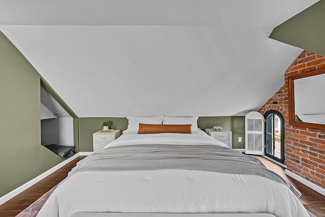 bedroom with brick wall, baseboards, vaulted ceiling, and wood finished floors