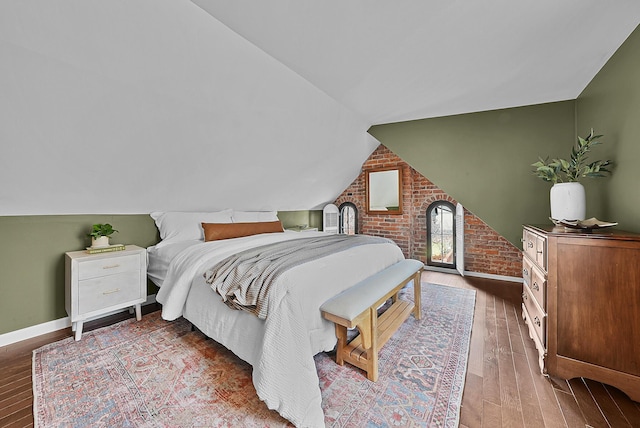 bedroom featuring vaulted ceiling, brick wall, wood finished floors, and baseboards