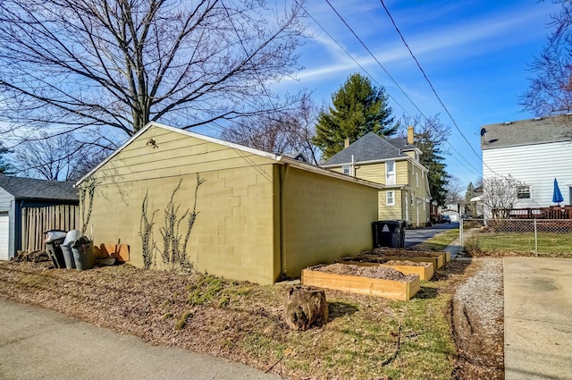 view of side of home with an outdoor structure, concrete block siding, and fence