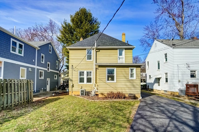 rear view of house with a yard, fence, a chimney, and central air condition unit