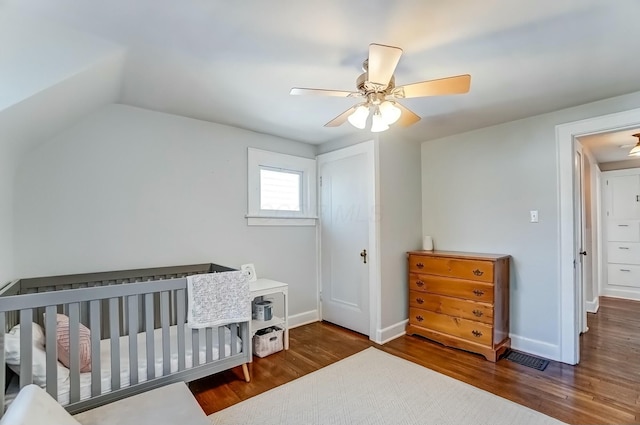 bedroom featuring lofted ceiling, ceiling fan, wood finished floors, baseboards, and a crib