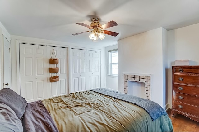 bedroom with dark wood-style floors, a fireplace, two closets, a ceiling fan, and baseboards