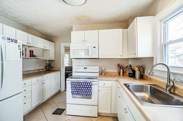 kitchen with light tile patterned floors, light countertops, white cabinetry, a sink, and white appliances