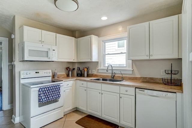 kitchen with light tile patterned floors, white appliances, a sink, white cabinets, and light countertops