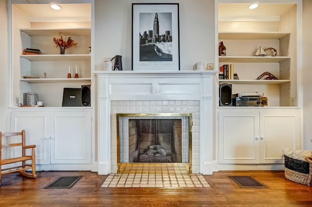 living area with built in shelves, a tile fireplace, visible vents, and wood finished floors