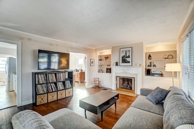 living area with dark wood-style floors, baseboards, a fireplace, and built in shelves