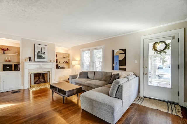 living room featuring built in shelves, hardwood / wood-style flooring, visible vents, ornamental molding, and a tiled fireplace