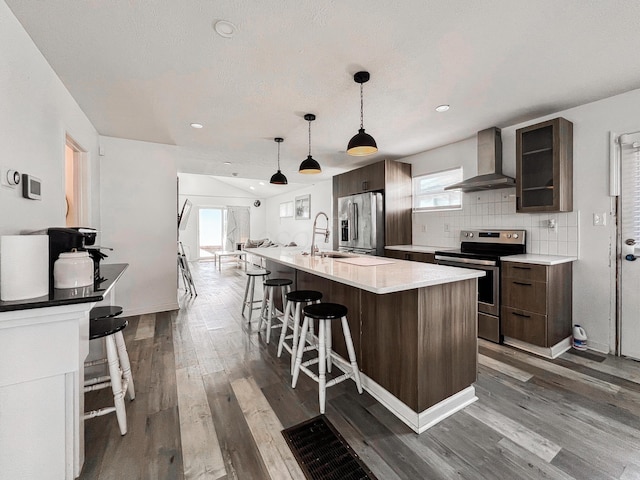 kitchen with a breakfast bar area, decorative backsplash, appliances with stainless steel finishes, a sink, and wall chimney exhaust hood