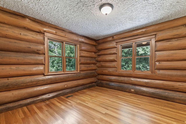 empty room with a textured ceiling, plenty of natural light, wood finished floors, and rustic walls