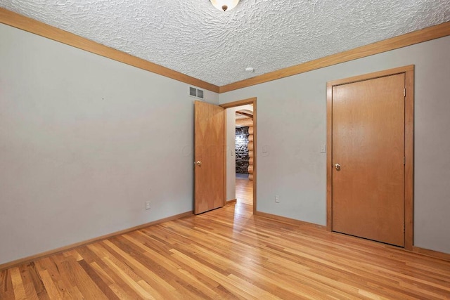 unfurnished bedroom featuring baseboards, visible vents, a textured ceiling, and light wood finished floors