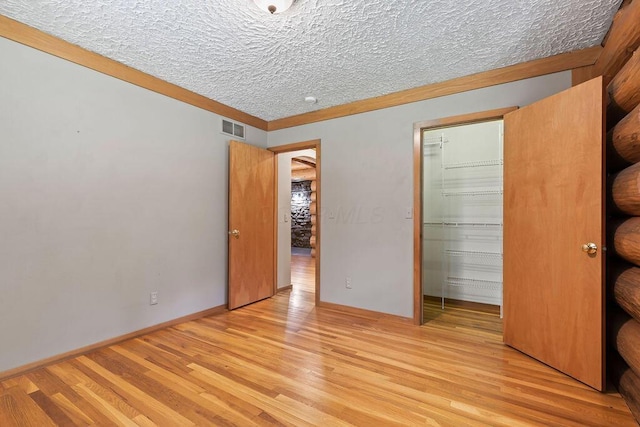 unfurnished bedroom featuring a textured ceiling, visible vents, light wood-style floors, a closet, and a walk in closet