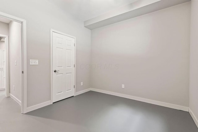 spare room featuring finished concrete flooring and baseboards