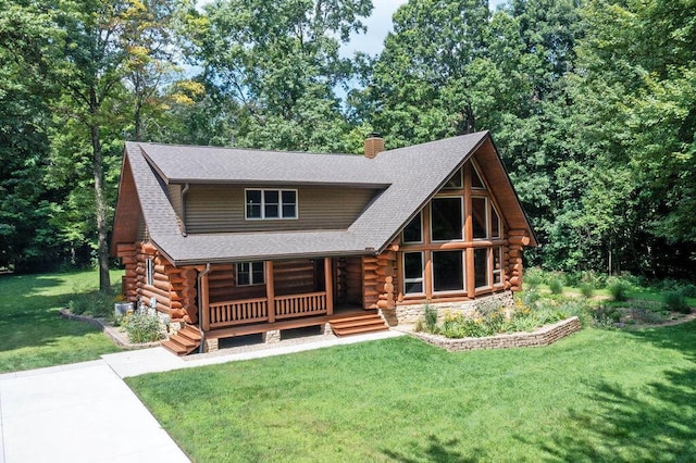 log cabin with a shingled roof, log exterior, a chimney, covered porch, and a front lawn