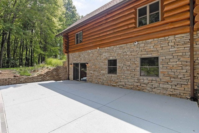 view of home's exterior featuring a patio, log exterior, and stone siding