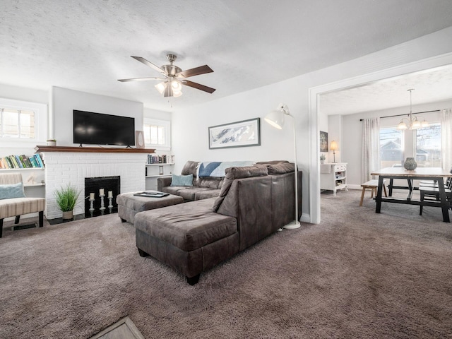 carpeted living area featuring ceiling fan with notable chandelier, a fireplace, baseboards, and a textured ceiling