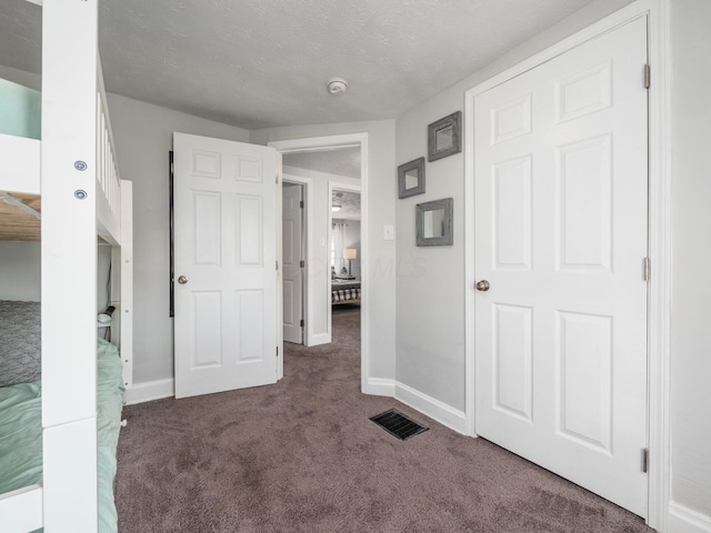 hallway featuring a textured ceiling, carpet, visible vents, and baseboards