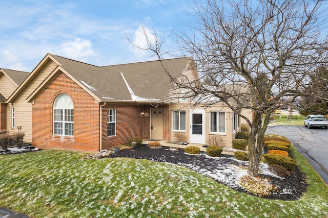 view of front of property featuring brick siding, a front yard, and roof with shingles