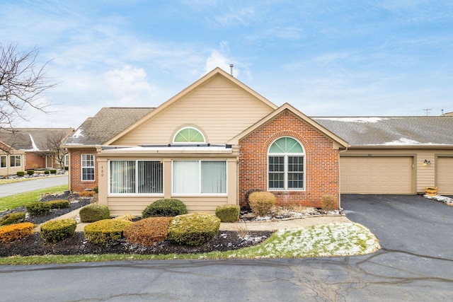 ranch-style house with aphalt driveway, a garage, brick siding, and roof with shingles