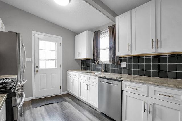 kitchen featuring lofted ceiling, a sink, white cabinets, appliances with stainless steel finishes, and tasteful backsplash
