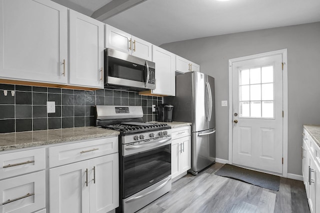kitchen featuring light stone counters, stainless steel appliances, white cabinetry, light wood-style floors, and backsplash