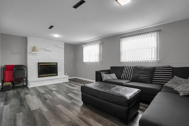 living room featuring visible vents, a stone fireplace, a textured ceiling, and wood finished floors