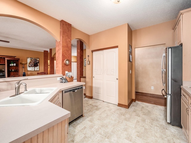 kitchen featuring arched walkways, appliances with stainless steel finishes, light countertops, a textured ceiling, and a sink