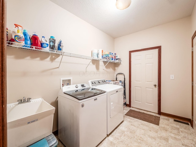 laundry room with washing machine and clothes dryer, visible vents, a sink, laundry area, and baseboards