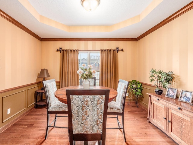 dining space with a tray ceiling, wainscoting, light wood-style flooring, and crown molding