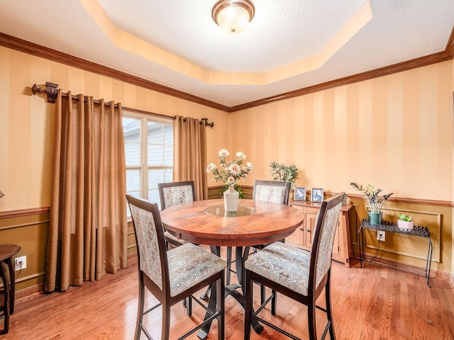 dining area with light wood-type flooring, wallpapered walls, a tray ceiling, and ornamental molding