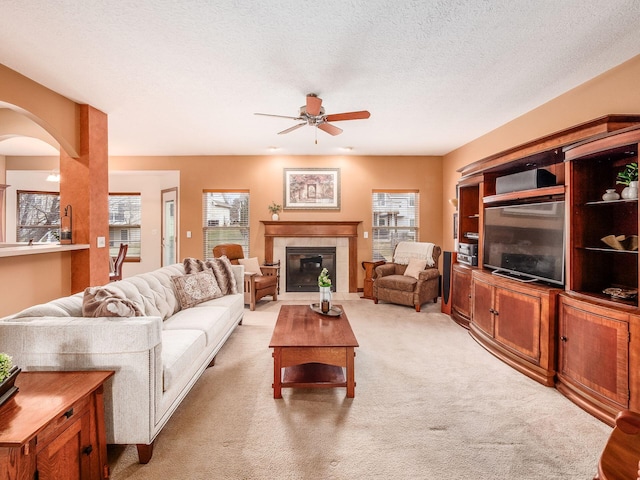 living room with arched walkways, light colored carpet, ceiling fan, a textured ceiling, and a fireplace