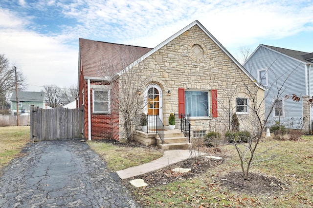 view of front of home with aphalt driveway, brick siding, fence, stone siding, and roof with shingles