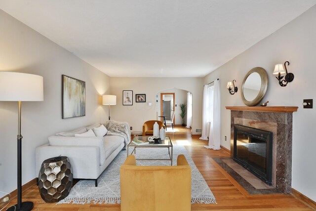 living room featuring arched walkways, baseboards, a fireplace, and light wood finished floors