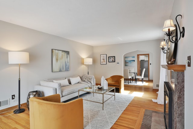 living room with arched walkways, baseboards, visible vents, and light wood-style floors