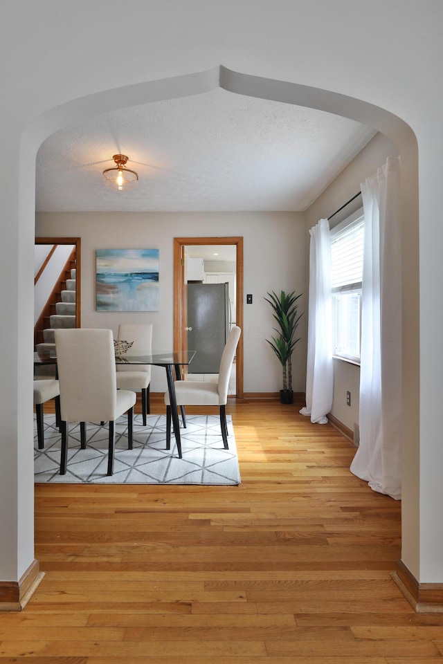 dining area with arched walkways, stairway, light wood-style flooring, a textured ceiling, and baseboards