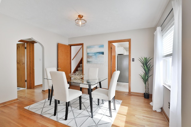 dining space featuring arched walkways, light wood finished floors, and baseboards